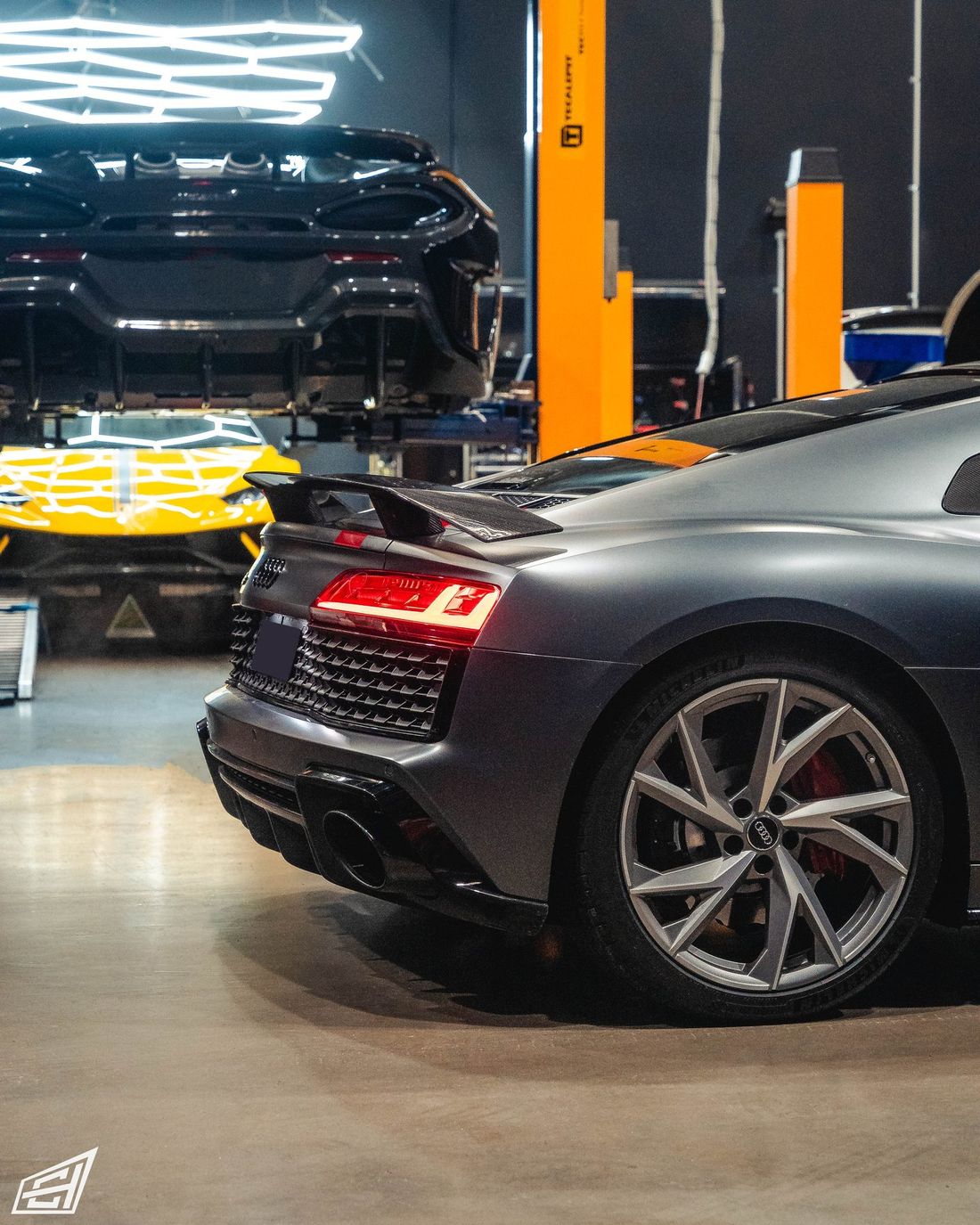 Grey Audi R8 V10 with a rear wing in the CADE Technologies workshop, with cars on hoists behind