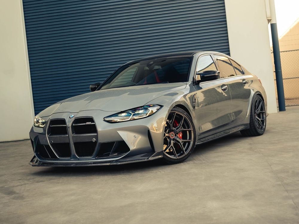 Grey BMW M3 (G80) with a carbon kidney grille and Vossen wheels parked in front of a roller door