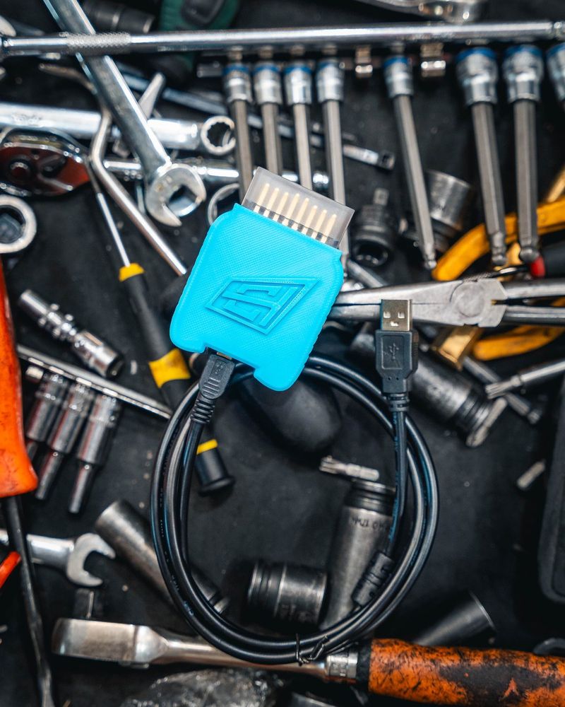 The blue CADE-FLASH OBD interface with its USB cable, resting on a bed of workshop tools