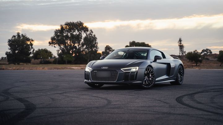 Matte grey Audi R8 V10 at dusk on an open tarmac lot, front three-quarter view