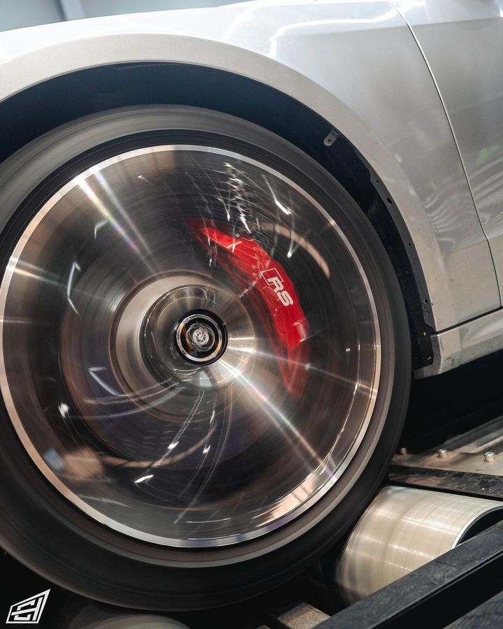 Wheel of a silver Audi spinning on the dyno rollers, with a red RS brake caliper