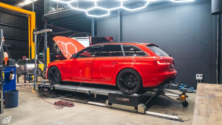Red Audi RS4 Avant strapped to the dyno under hexagonal workshop lights, bonnet raised