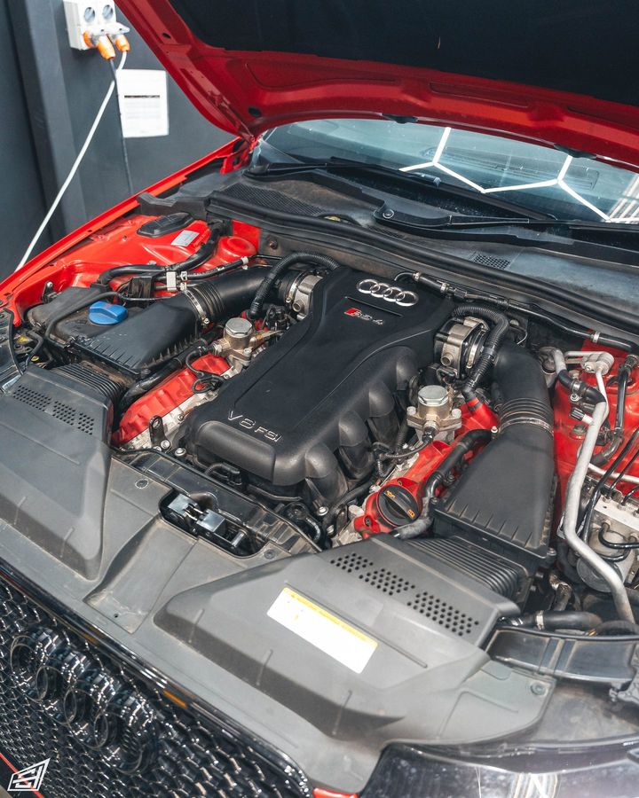 Engine bay of a red Audi RS4 with the bonnet open, showing the V8 FSI engine and red intake plenums