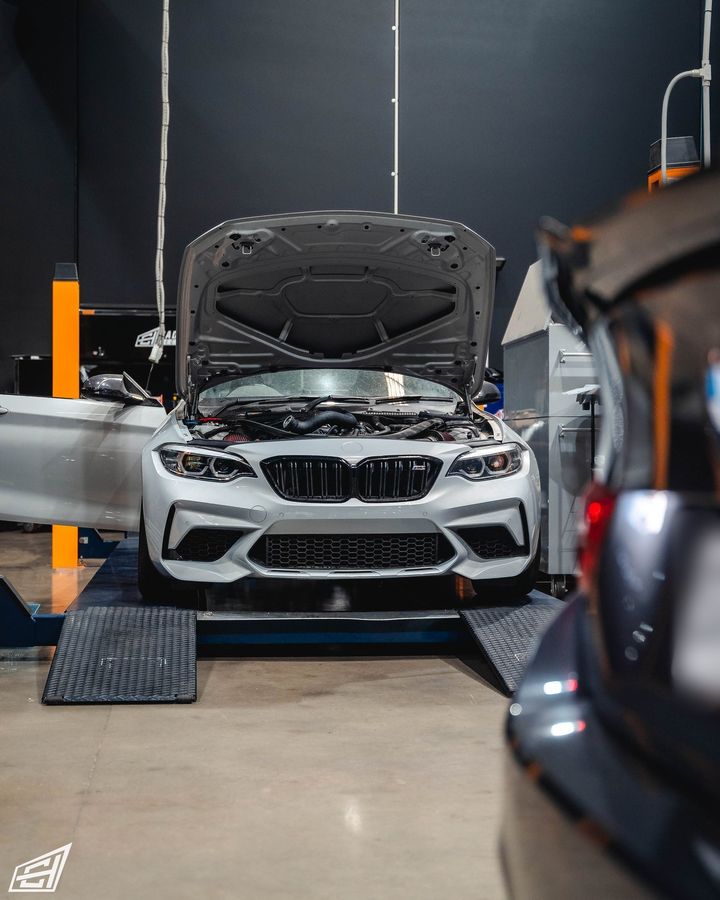 Silver BMW M2 Competition (F87) on a lift with its bonnet open in the CADE Technologies workshop