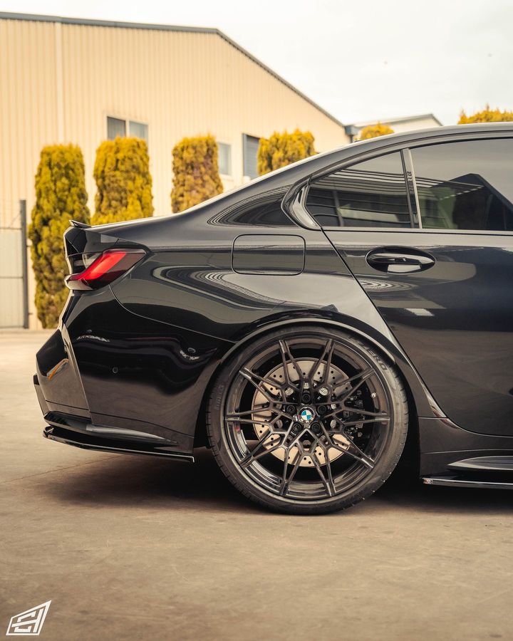 Rear three-quarter view of a black BMW M3 sedan outside the workshop, with dark forged wheels and a rear spoiler