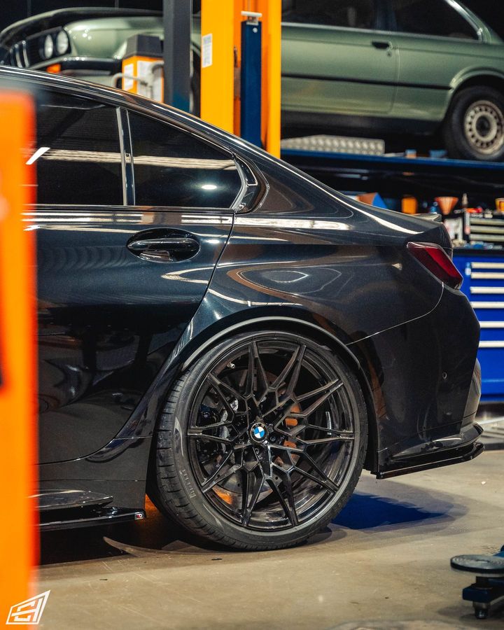 Black BMW M3 sedan in the workshop, rear three-quarter view of its forged wheel and flared arch