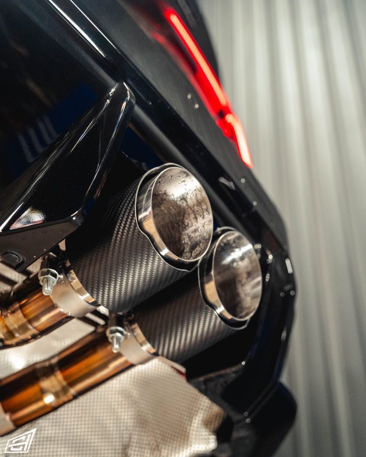 Close-up of carbon-fibre exhaust tips and titanium piping under the rear of a black car