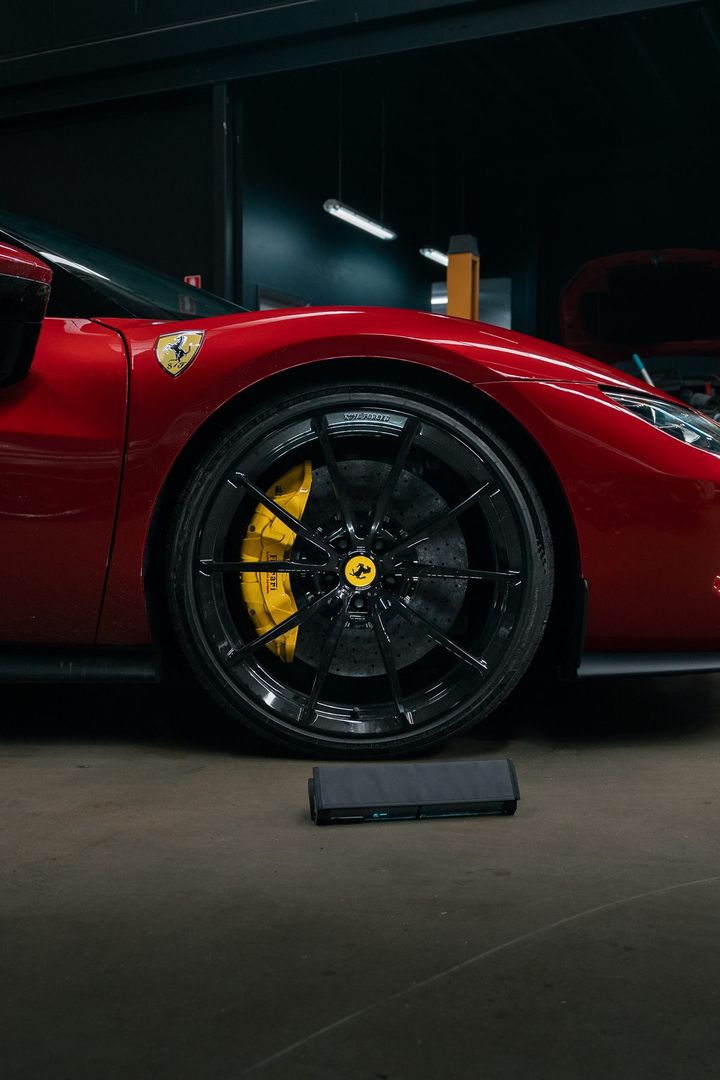 Front wheel of a red Ferrari with a black rim and yellow brake caliper, parked in the CADE Technologies workshop