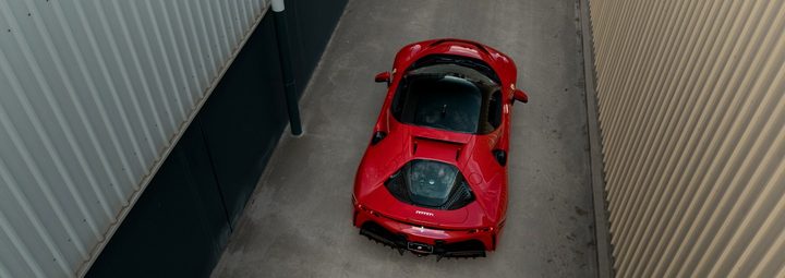 Red Ferrari SF90 Stradale seen from above and behind, parked in a concrete laneway between metal-clad buildings