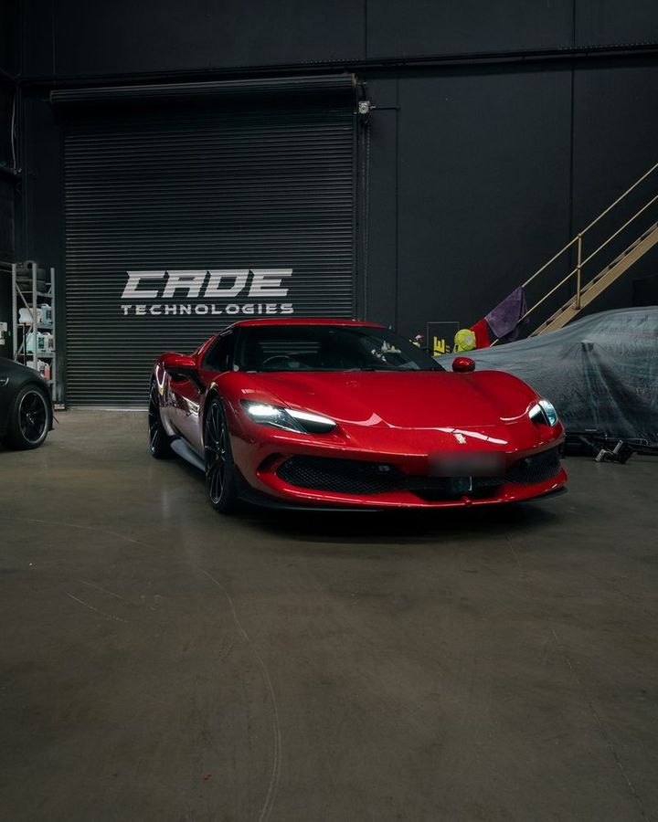 Red Ferrari 296 GTB in front of the illuminated CADE Technologies roller-door sign