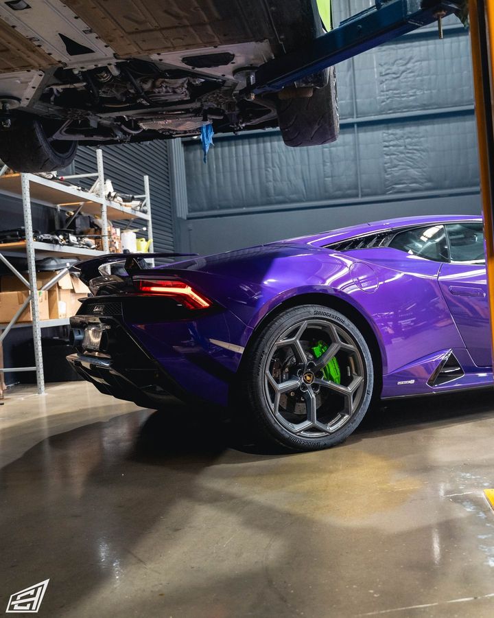 Purple Lamborghini Huracán with green brake calipers in the workshop, beneath a car on a hoist