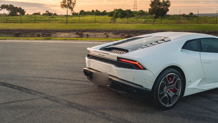 White Lamborghini Huracán parked on an open lot at sunset, rear three-quarter view