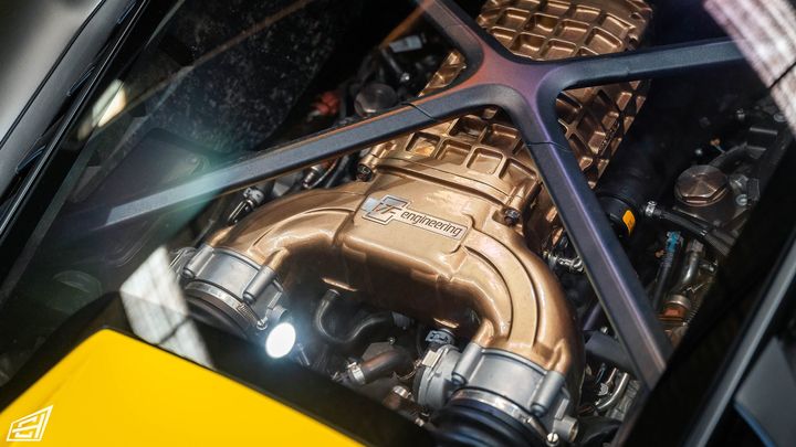 View through the engine cover of a yellow Lamborghini showing a bronze-finished supercharger installation