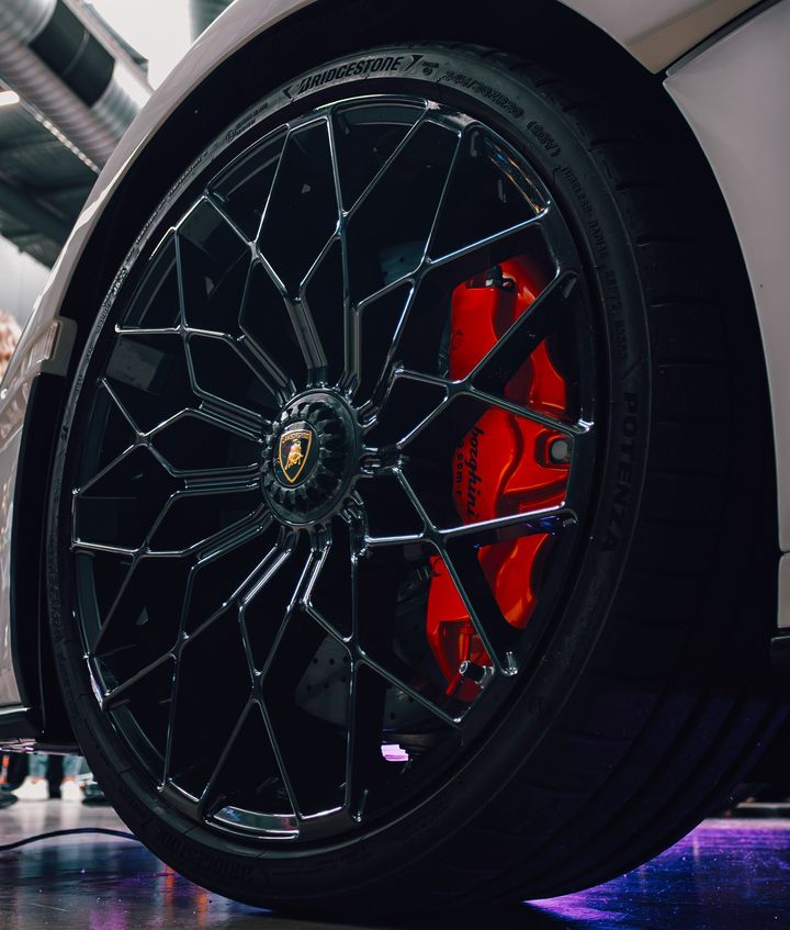 Low-angle close-up of a Lamborghini wheel with a black multi-spoke rim and red brake caliper