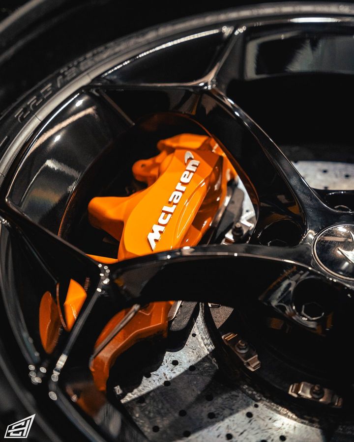Close-up of an orange McLaren brake caliper behind a black wheel