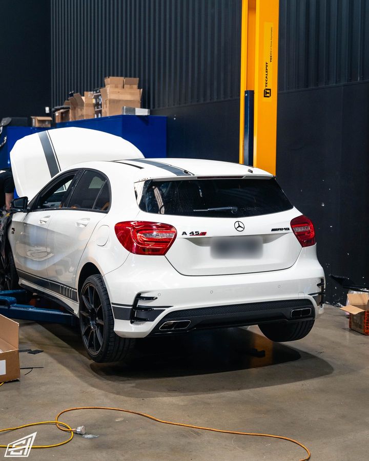 White Mercedes-AMG A 45 hatch with black stripes and its bonnet open in the workshop