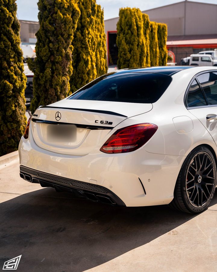 Rear three-quarter view of a white Mercedes-AMG C 63 S sedan with black wheels and a lip spoiler