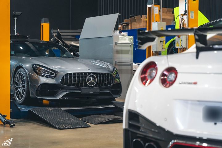 Grey Mercedes-AMG GT with Panamericana grille in the workshop, beside the rear of a white Nissan GT-R