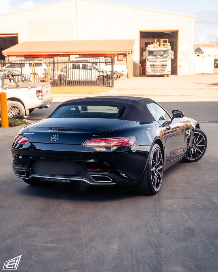 Black Mercedes-AMG GT Roadster with its soft top up, rear three-quarter view outside the workshop