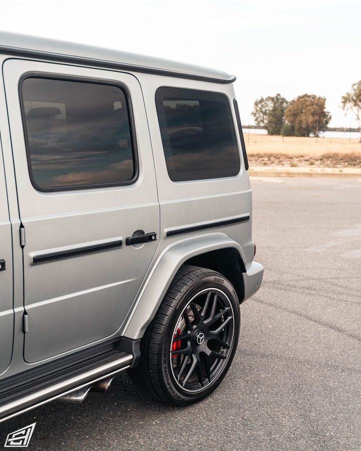 Side detail of a matte silver Mercedes G-Class with a black multi-spoke wheel and red brake caliper