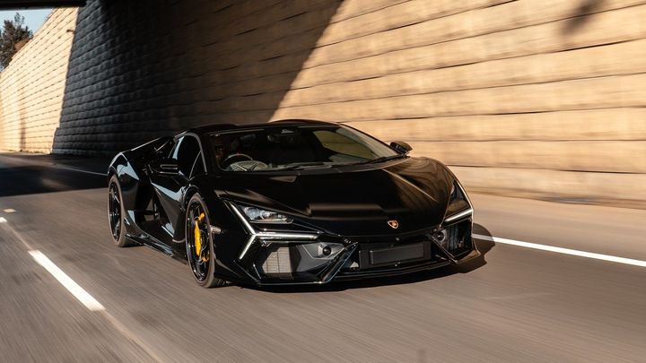 Black Lamborghini Revuelto with yellow brake calipers driving through a sunlit concrete underpass