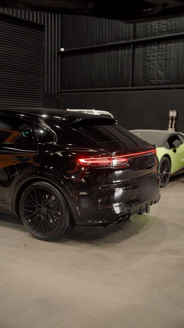 Rear three-quarter view of a black Porsche SUV with dark wheels inside the workshop
