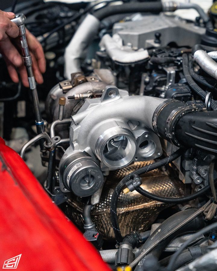 Technician working on a turbocharger in an engine bay, with a red wing cover in the foreground