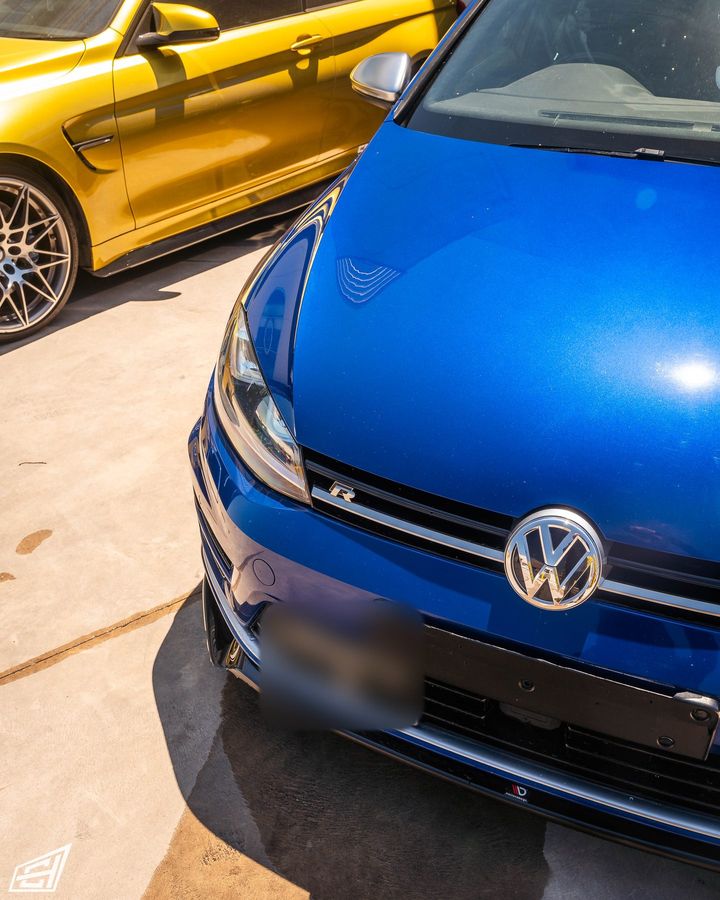 Front of a blue Volkswagen Golf R parked next to a yellow BMW