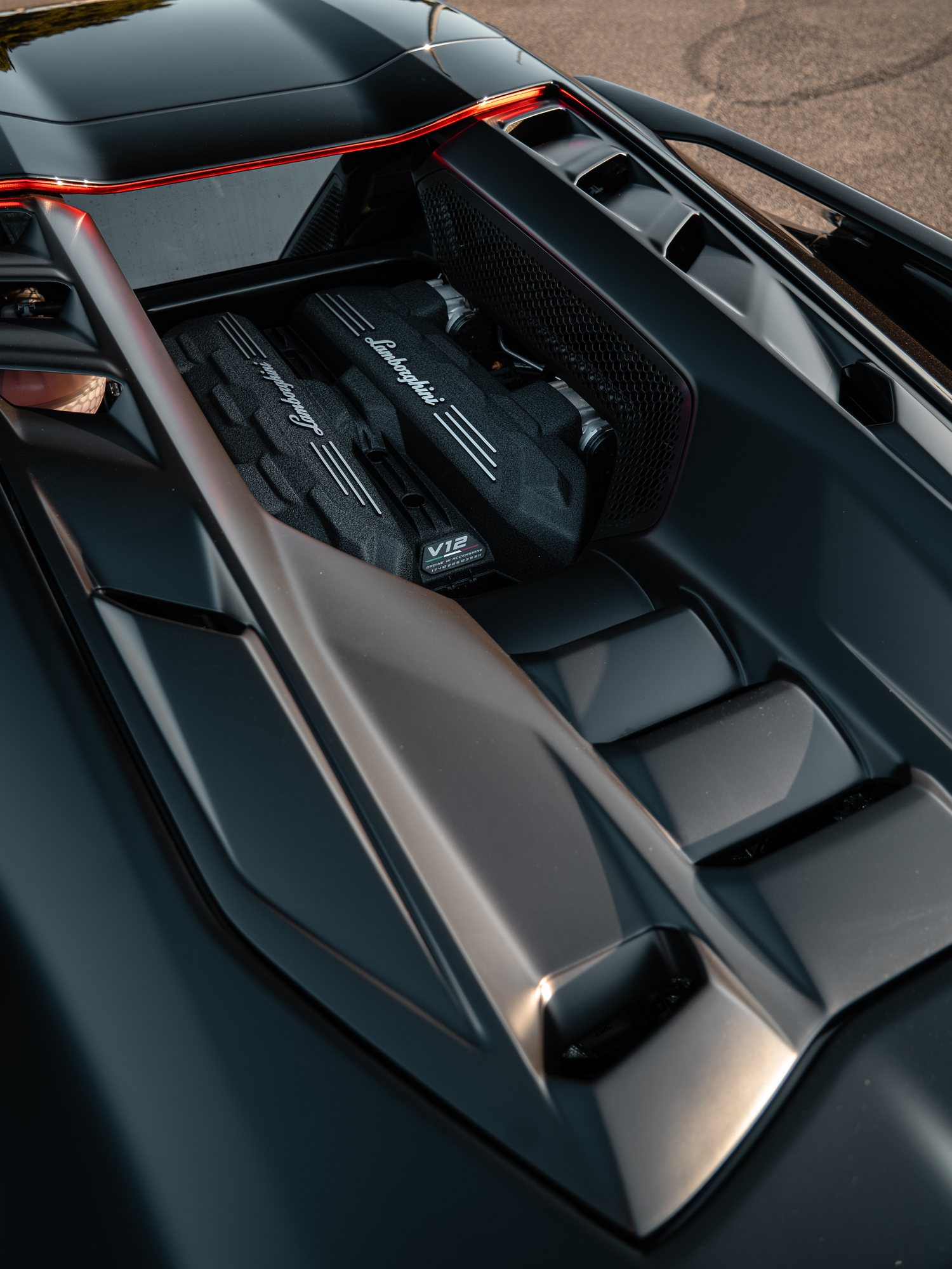 High rear view into the open engine bay of a black Lamborghini Revuelto, showing its textured engine covers with Lamborghini script and a V12 badge