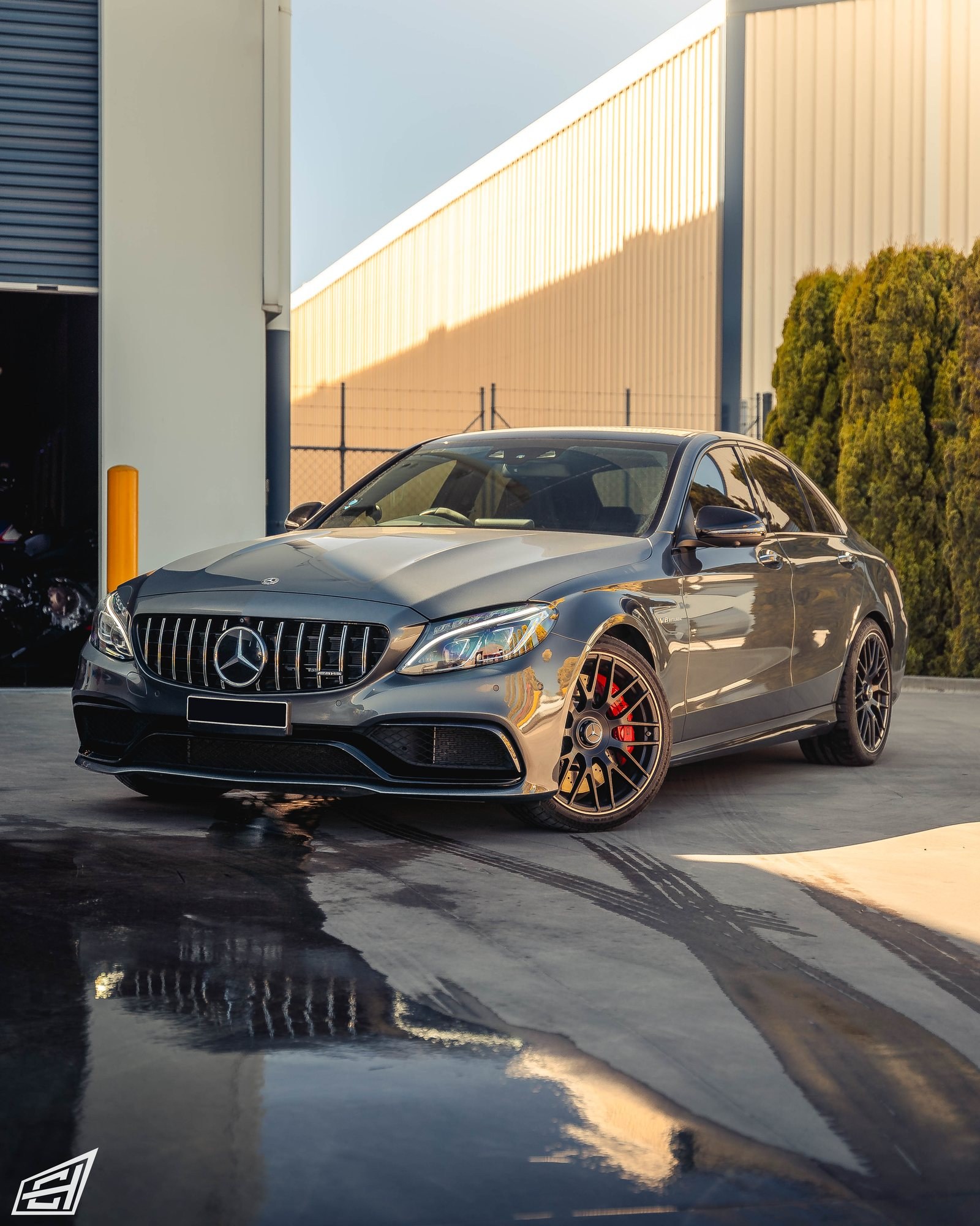 Grey Mercedes-AMG C 63 S sedan (W205) with red brake calipers outside the workshop, front three-quarter view