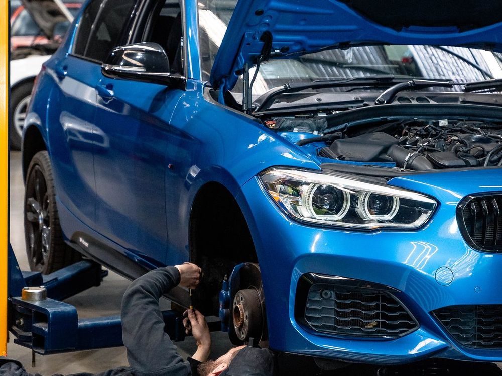 CADE technician working at the front wheel of a blue BMW 1 Series raised on the hoist, bonnet open