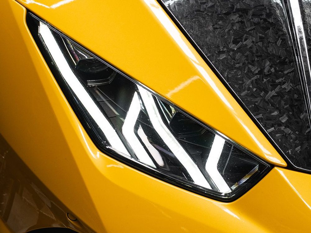 Close-up of a yellow Lamborghini Huracán EVO headlight and forged-carbon bonnet under hexagonal workshop lights