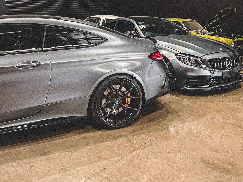 Two matte grey Mercedes-AMG C63 coupes in a workshop