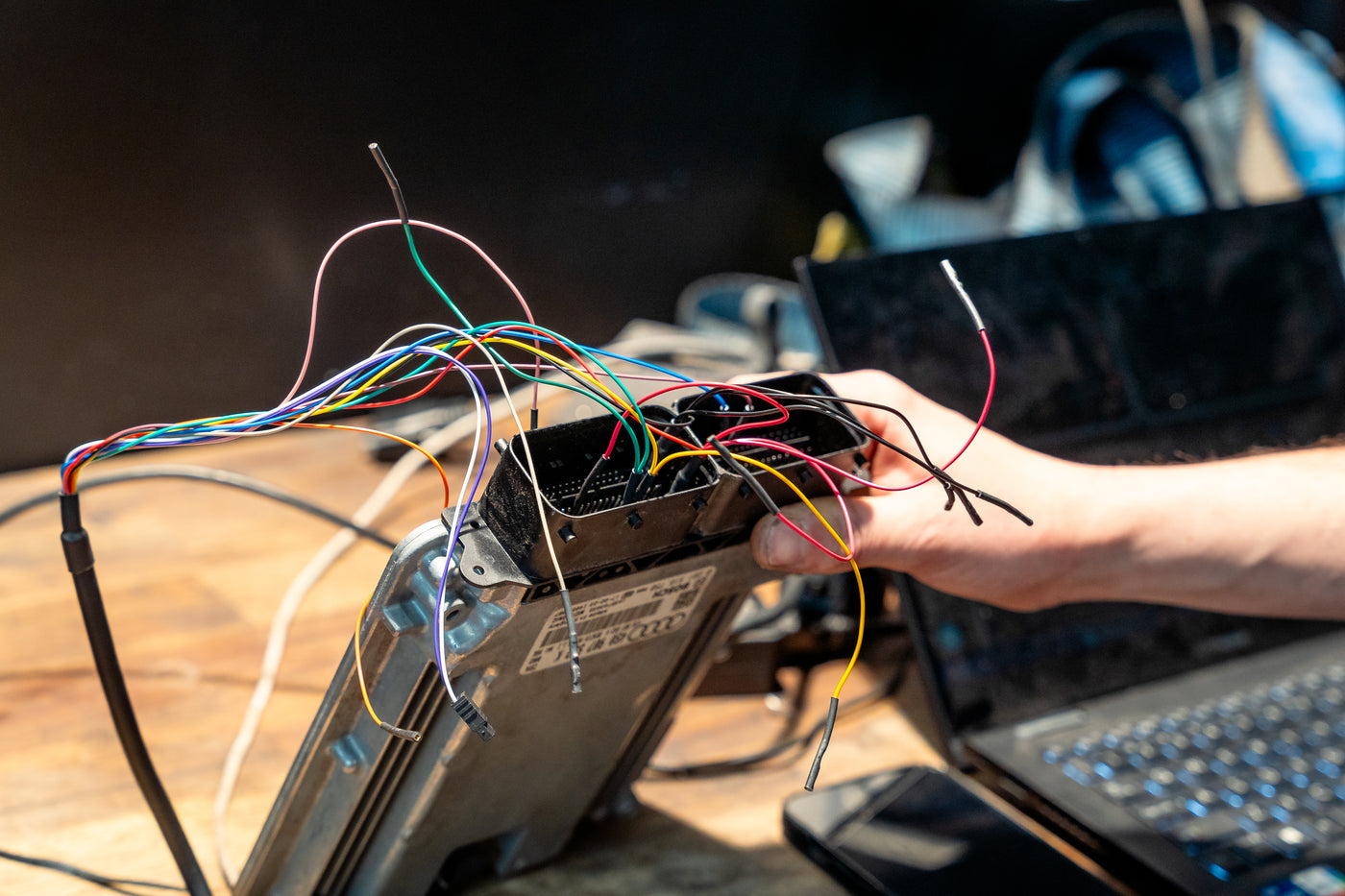 ECU opened on the bench with its wiring harness connected and a laptop alongside