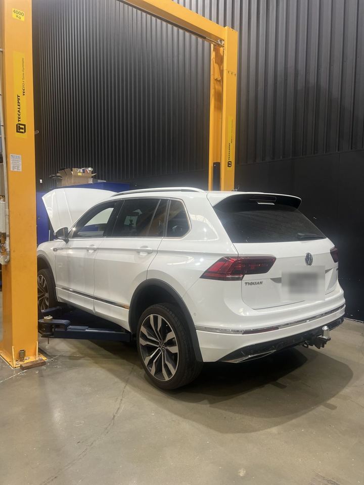 White Volkswagen Tiguan raised on the hoist in the CADE Technologies workshop, rear three-quarter view