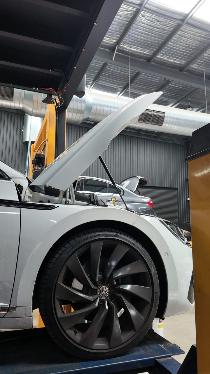 White Volkswagen raised on a two-post hoist with its bonnet open in the CADE Technologies workshop